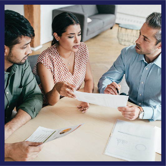 A group of 3 people talking and looking at a document together.