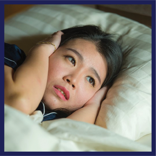 A person lying in bed. They are awake and are covering their ears with their hands.