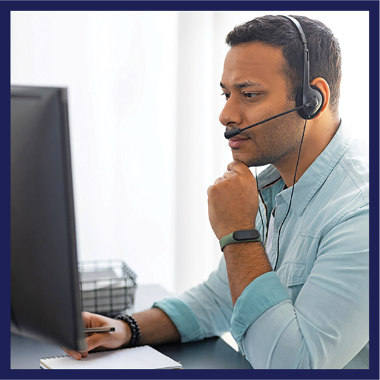 A person looking at a computer. They have a phone headset on.